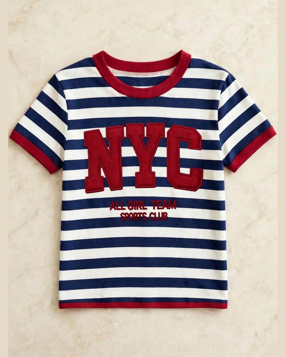 Blusa de rayas azul/blanco con bordado rojo 'NYC', aislada (gancho, gráfico con texto y collar eliminados) sobre mármol marfil