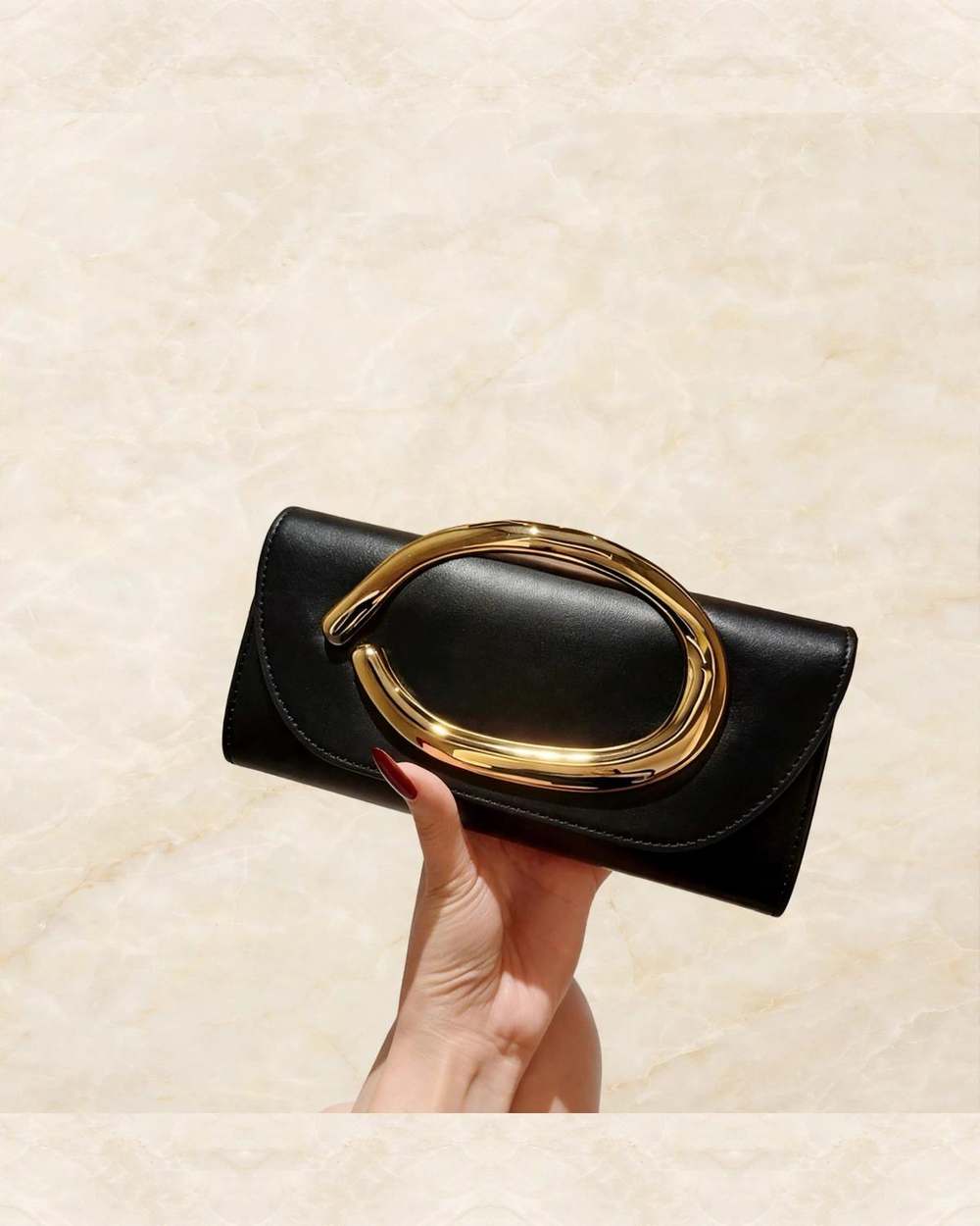 Clutch negro con asa dorada tipo argolla., aislado sobre mármol marfil