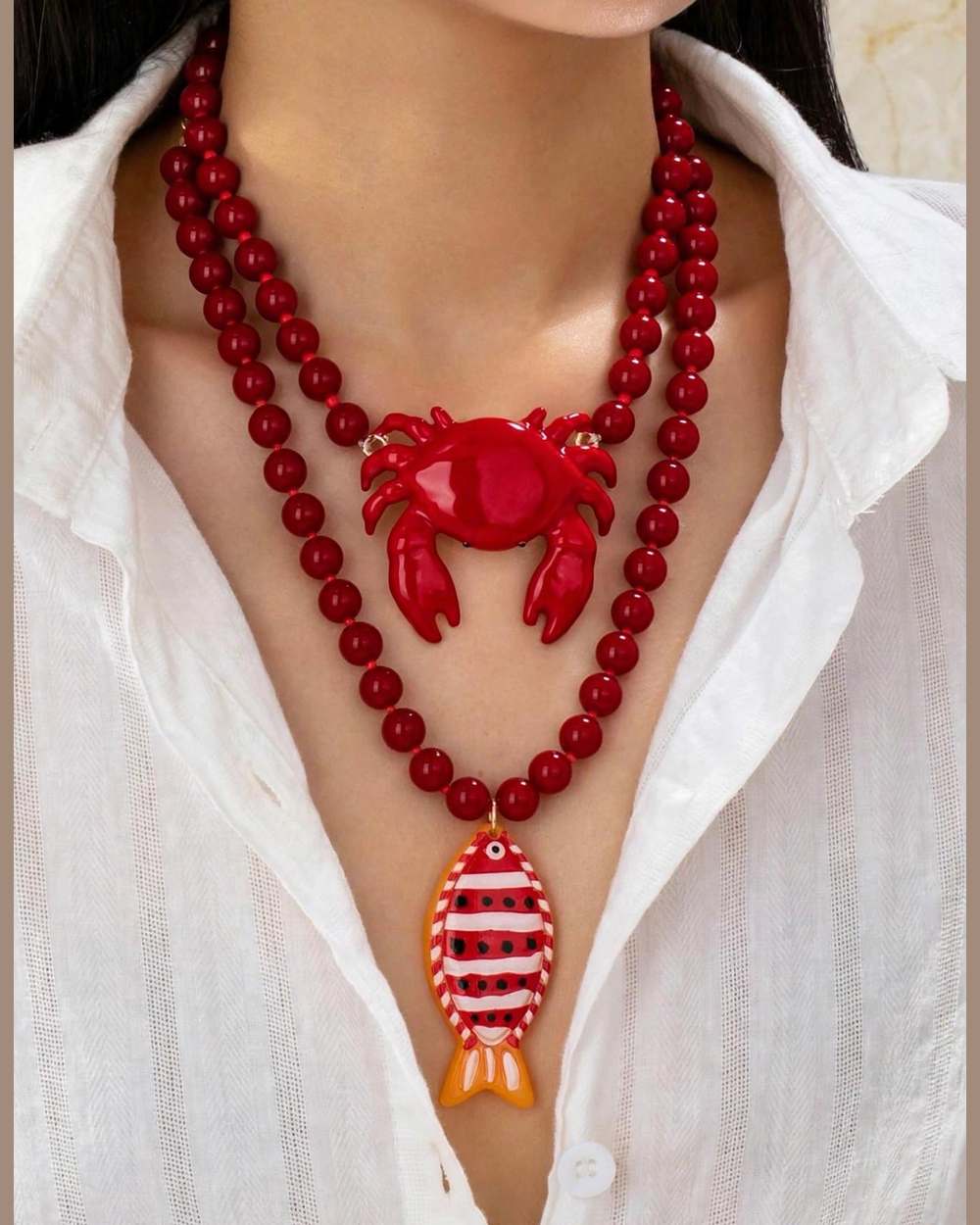 Modelo con collar de perlas rojas con dije de cangrejo y pez