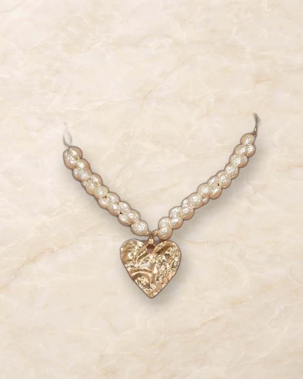 Collar de perlas con dije de corazon dorado., aislado sobre mármol marfil