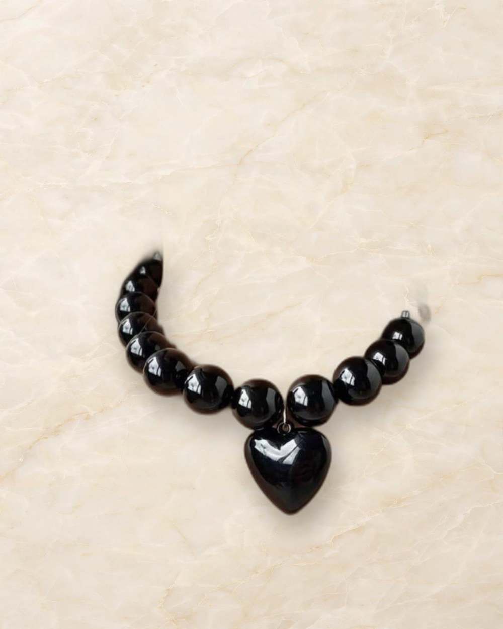 Collar de perlas negras con dije de corazon negro., aislado sobre mármol marfil