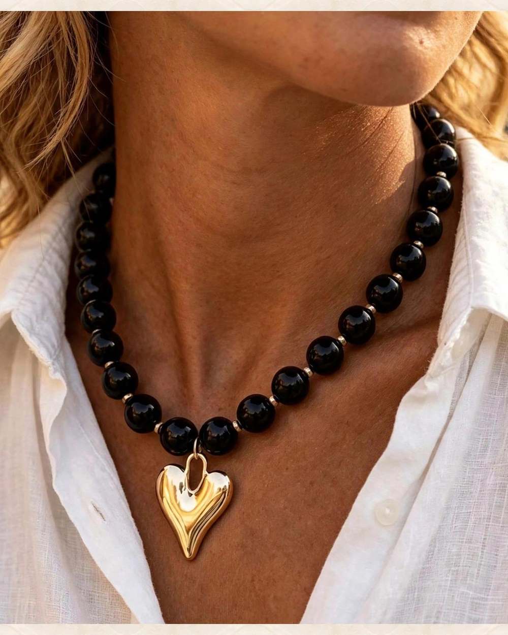 Collar de perlas negras con dije de corazon dorado., aislado sobre mármol marfil