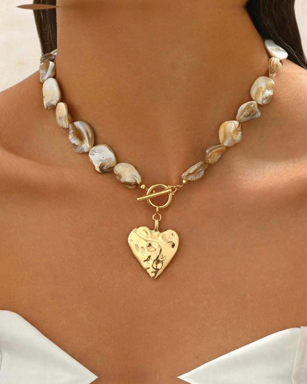Collar nacar corazon dorado, aislado sobre mármol marfil