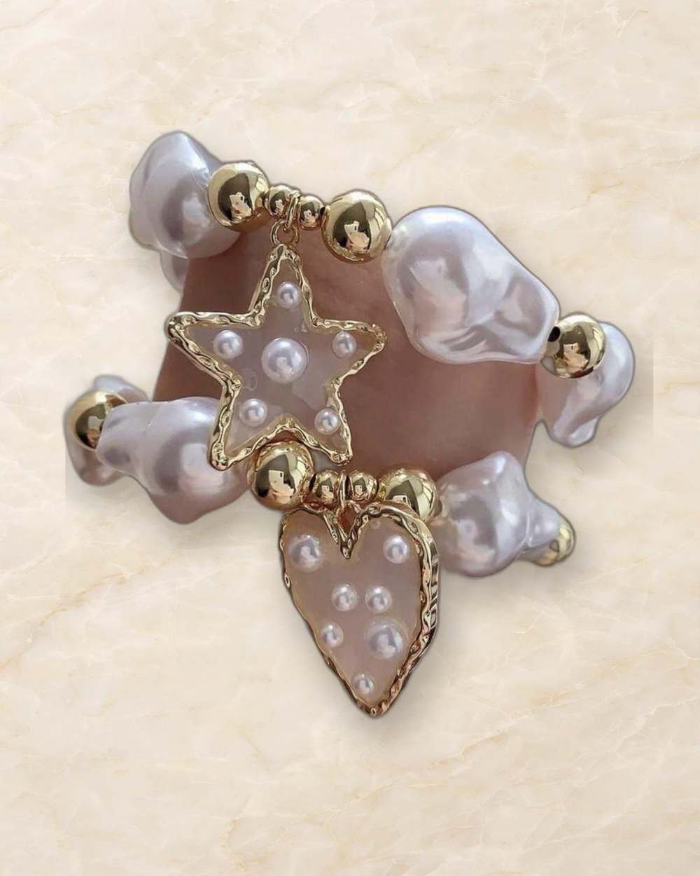Pulsera de perlas con dijes de estrella y corazon dorados., aislado sobre mármol marfil
