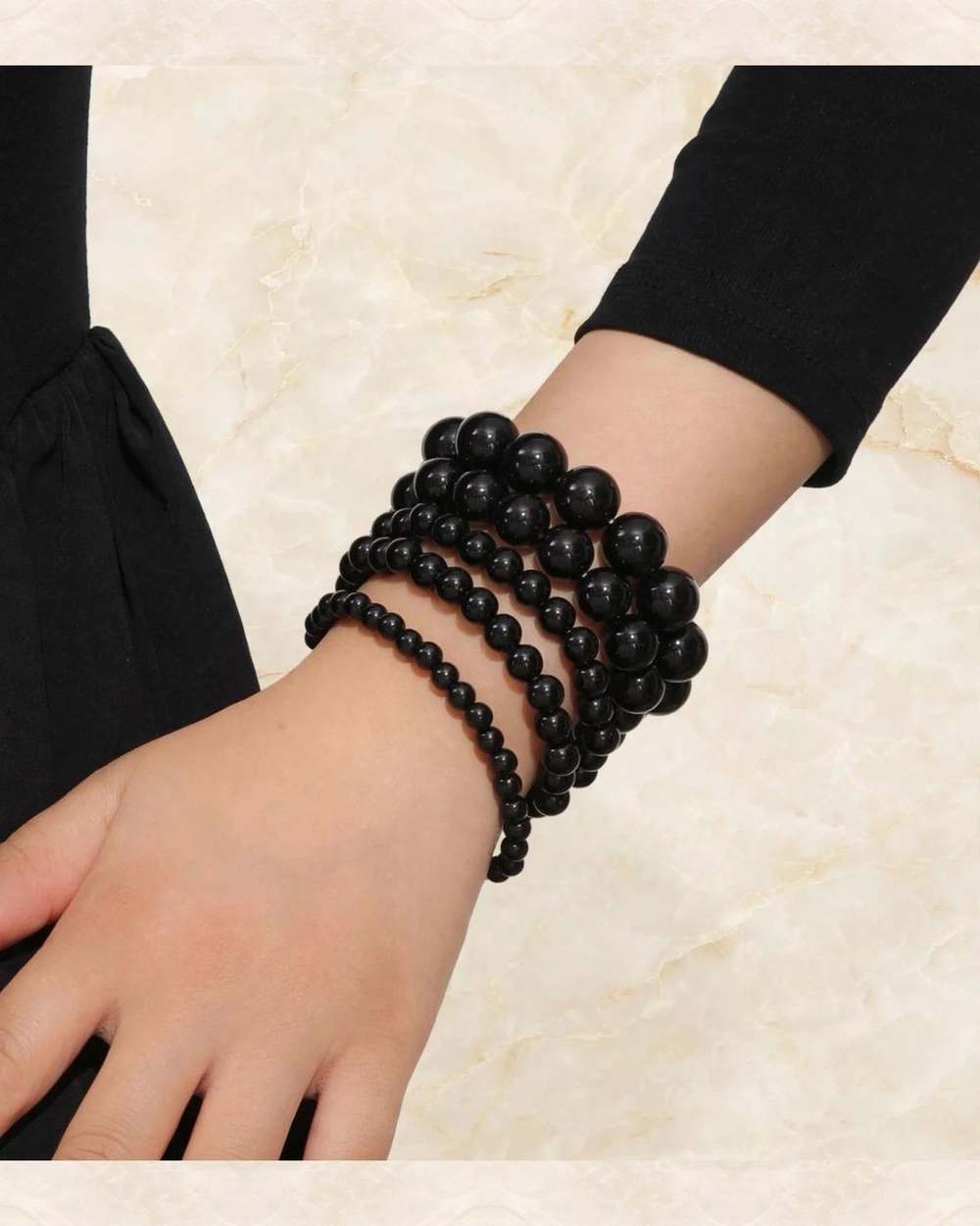 Juego de pulseras apiladas de perlas negras., aislado sobre mármol marfil