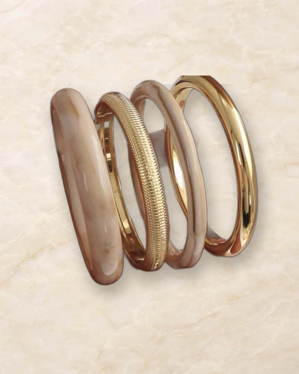 Set pulseras bangas beige doradas, aislado sobre mármol marfil
