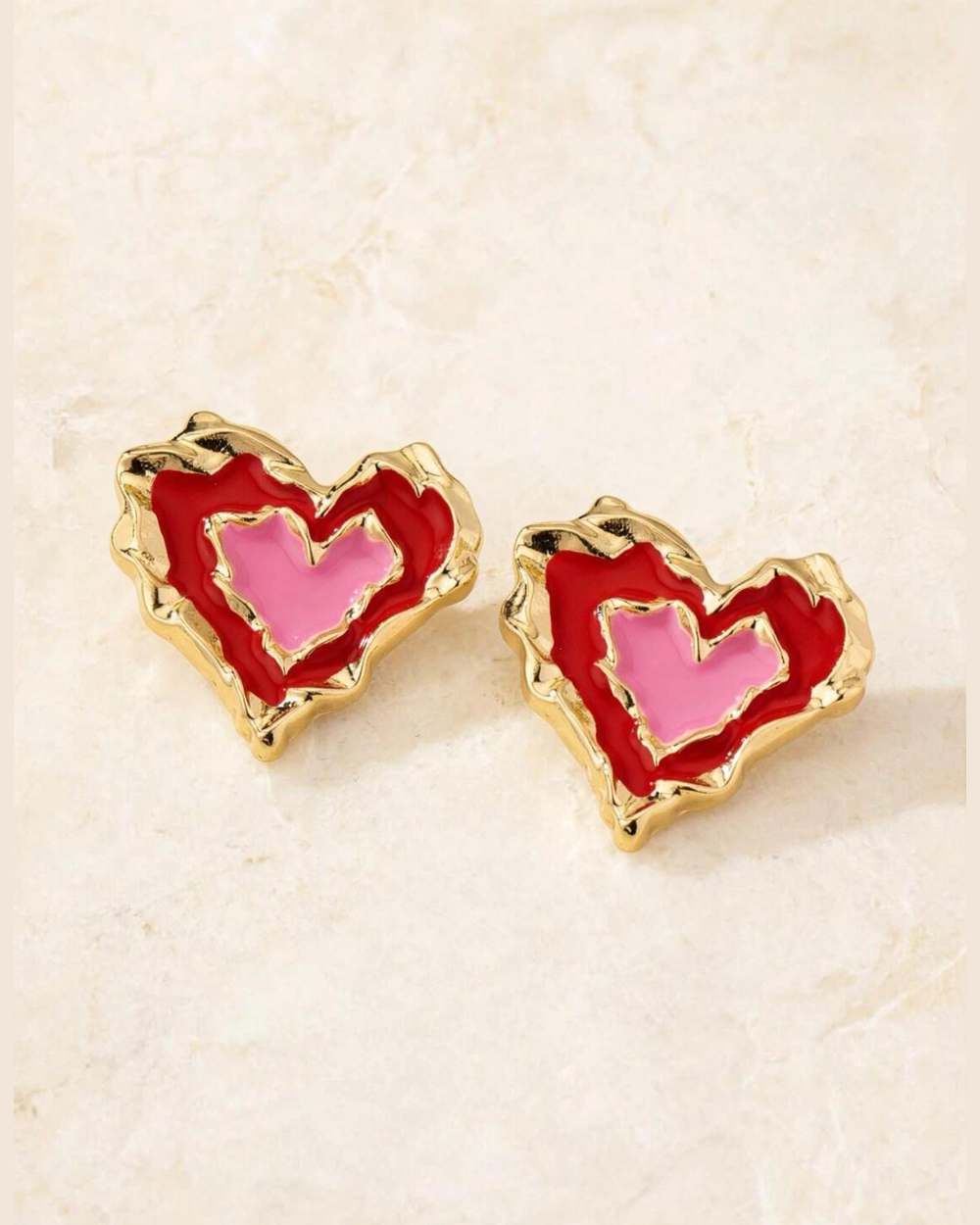 Zarcillos de corazón dorado con esmalte rojo/rosa, aislados (estuche eliminado) sobre mármol marfil