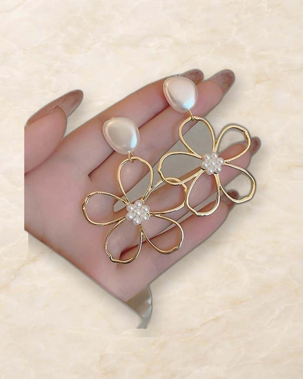 Zarcillos de flor con perla y detalles dorados., aislado sobre mármol marfil