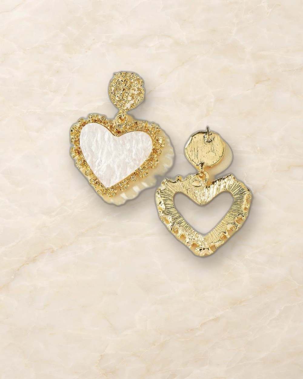 Zarcillos colgantes de corazon de nacar con marco dorado., aislado sobre mármol marfil